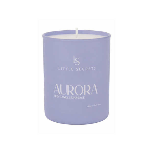 A lavender-colored wax candle in a matte cylindrical container with a white wick. The front of the container features white printed text reading 'LS LITTLE SECRETS AURORA SKIN CANDLE MASSAGE'.