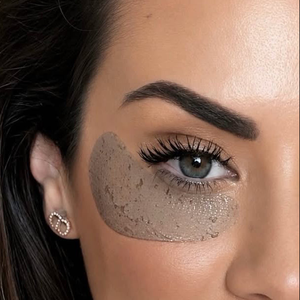 Close-up of a woman's face showing a textured, speckled beige makeup under-eye patch applied beneath her right eye.