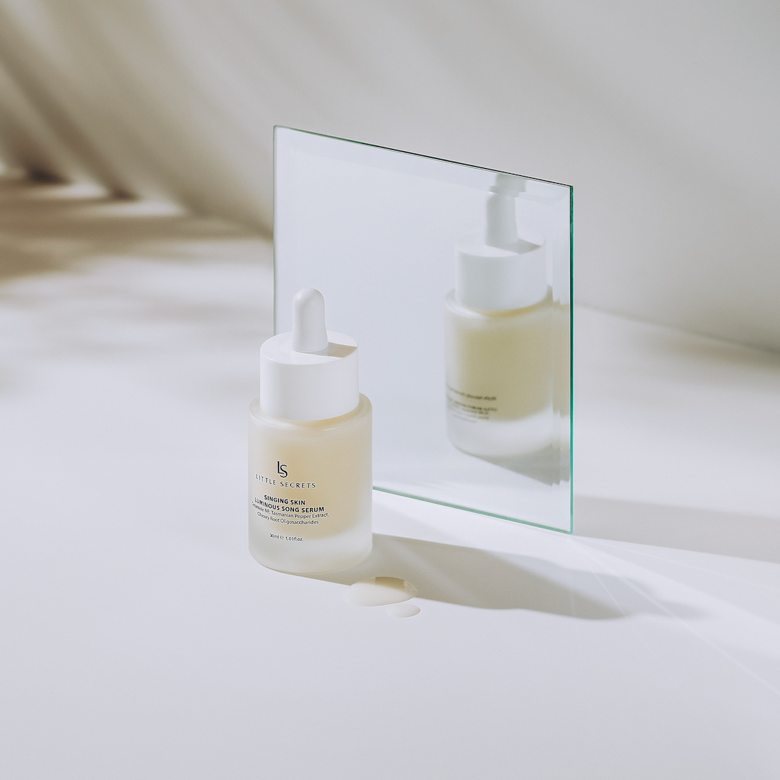 A frosted glass dropper bottle of SKIN1001 Snapping Skin Serum with a white dropper cap, styled on a white surface with a clear glass mirror reflecting its back, set against a soft beige background.