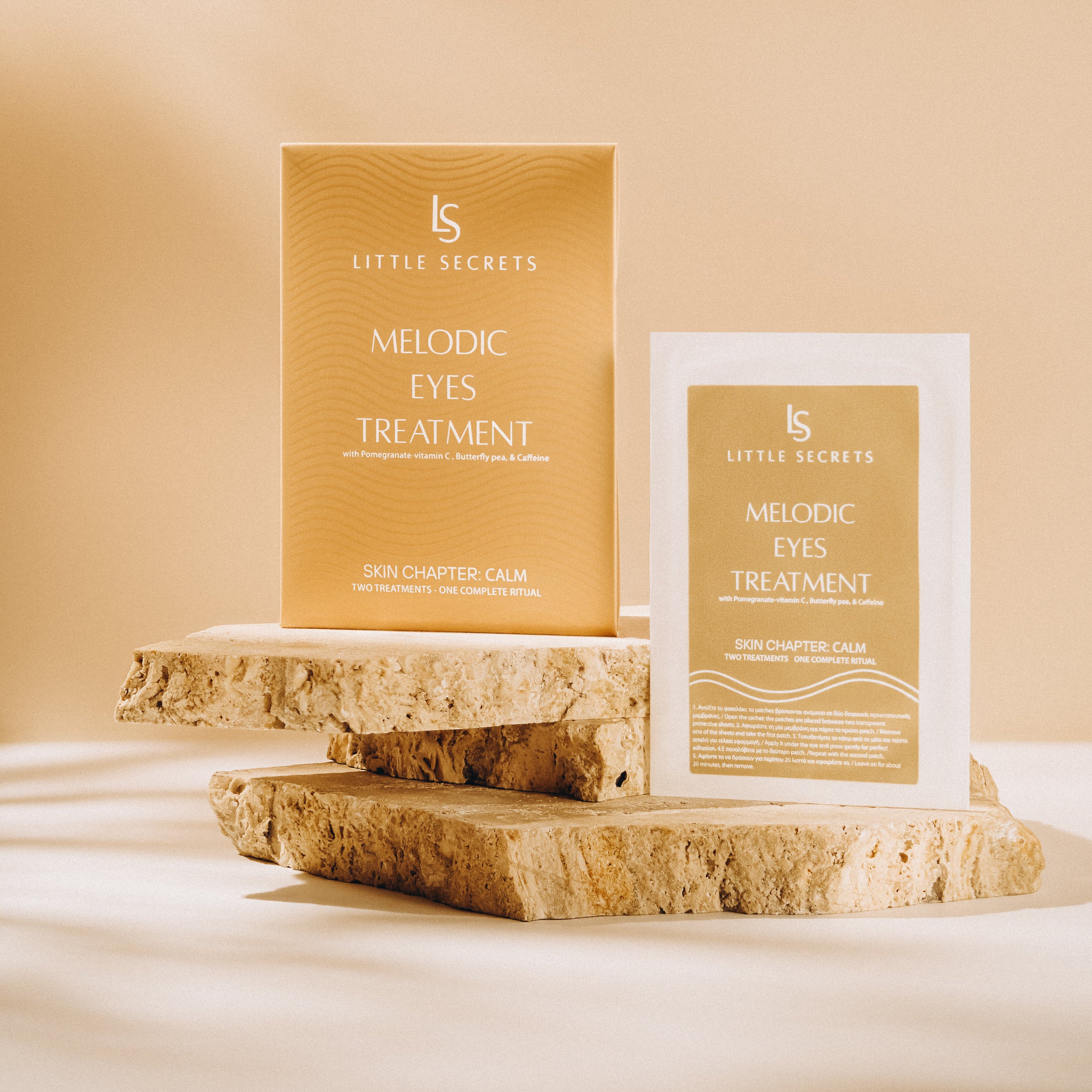 Little Secrets Melodic Eyes Treatment shown in its gold outer box and an individual single-use packet, styled on rustic stone slices against a warm beige background.